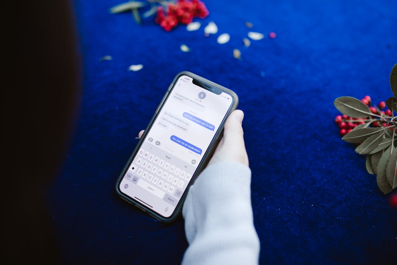 heros-img A person holding a smartphone displaying text messages on a blue surface with flowers.